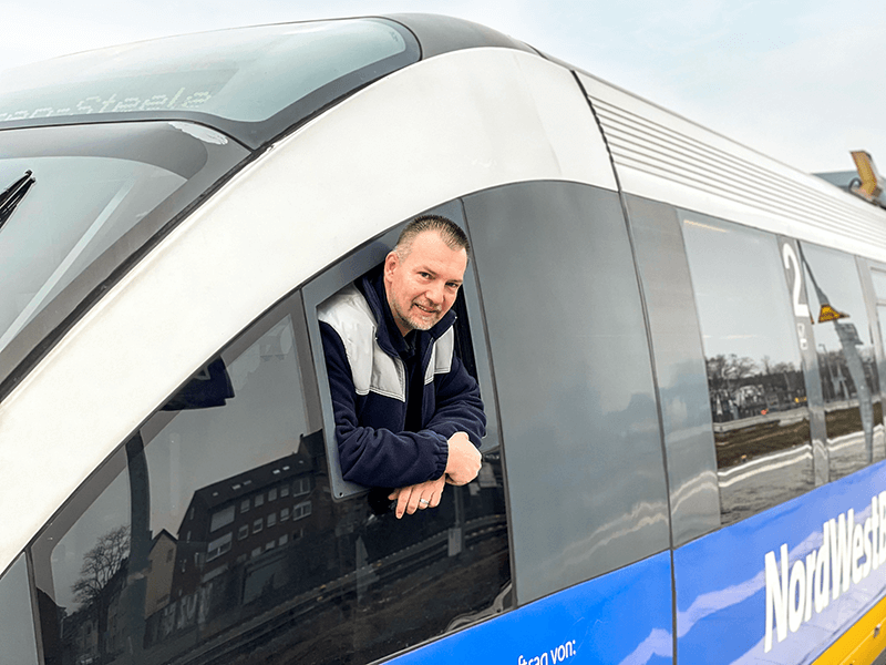 Ein Mann mit hellbraunen Haaren schaut aus dem Fenster eines Zuges. 