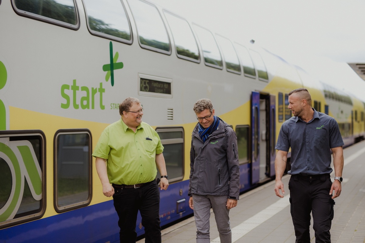 Ein Zug des Unternehmens Start Deutschland steht an einem Bahnhof, drei Mitarbeitende laufen davor herum. 