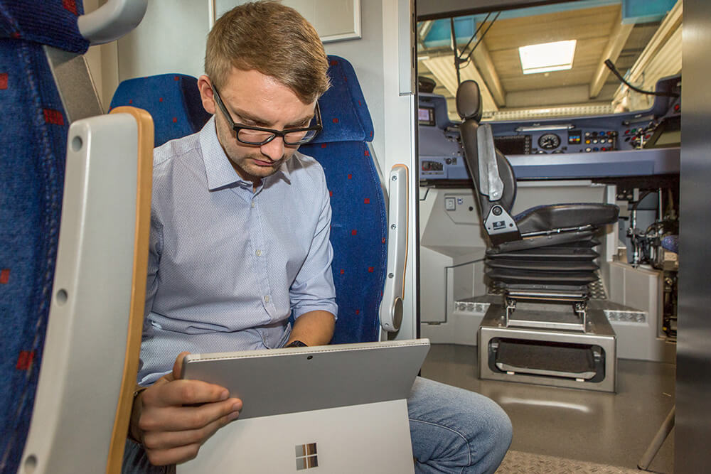 Ein Mitarbeiter schaut auf ein Tablet. Er sitzt in einem Zug und die Tür zum Führerstand steht offen.