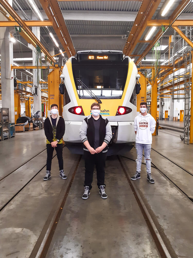 Drei junge Männer stehen vor der einem Zug der eurobahn in der Werstatt.