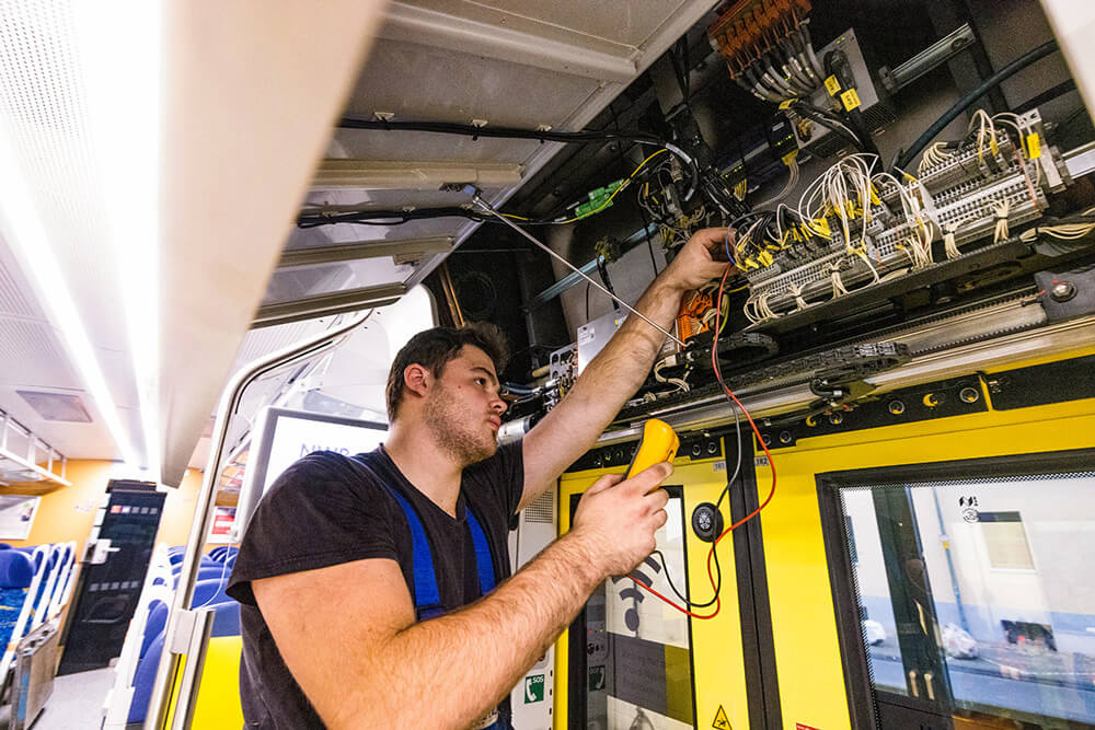 Junger Mann in Handwerker-Outfit arbeitet an der Türelektronik in einer Bahn.