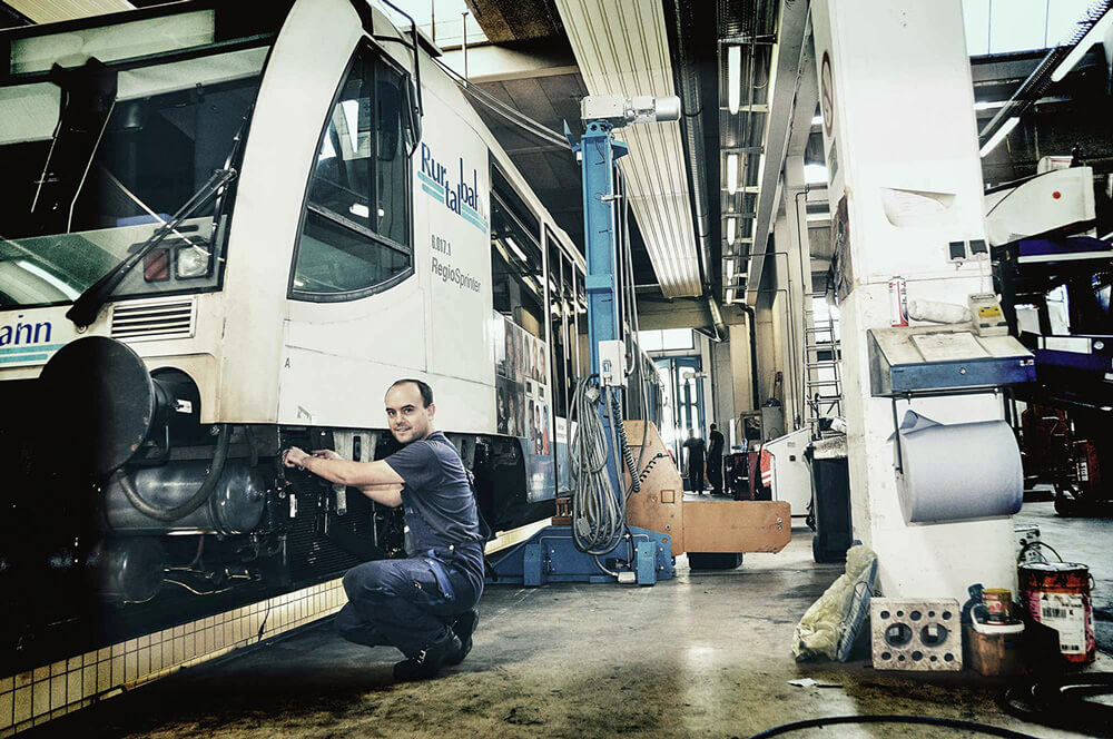 Ein Mann im Blaumann hockt in der Werkstatt neben einem Zug.