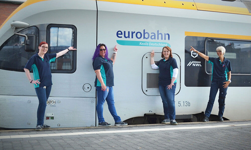 Vier Lokführerinnen der eurobahn stehen vor einem Zug und zeigen auf das angebrachte Logo des Unternehmens.