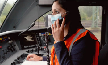 Eine Frau in Arbeitskleidung, die in Warnweste im Cockpit sitzt und telefoniert.