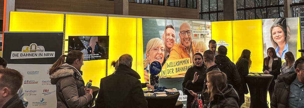 Ein gelber Messestand mit Fotos der Bahnfamilie.