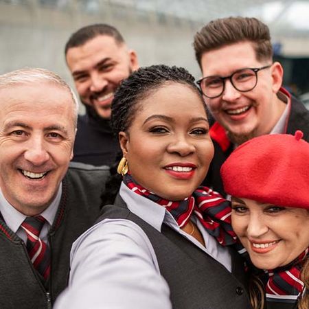 Eine Frau mit dunklen Haaren macht ein Selfie gemeinsam mit ihren Kolleg*innen – alle lächeln gemeinsam in die Kamera.