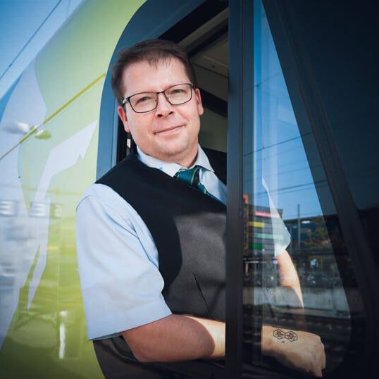 Ein Lokführer schaut aus dem Fenster im Führerstand, die Sonne scheint.