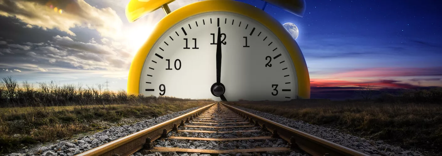 Ansicht einer Schienentrasse. Am Himmel ist eine Uhr zu sehen, deren Zeiger genau auf 12 Uhr steht. Auf der linken Seite des Bildes geht die Sonne auf, auf der rechten Seite geht sie unter.