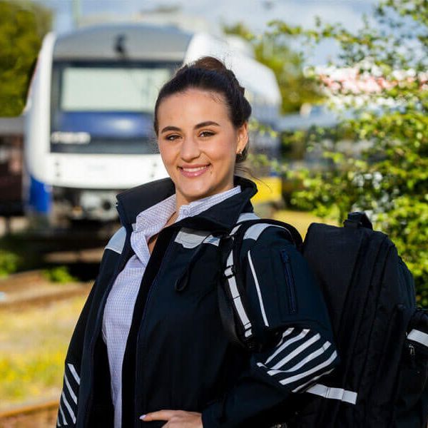 Junge Frau in Bahn-Uniform schaut in die Kamera. Im Hintergrund sieht man einen Regionalexpress auf einem Abstellgleis.