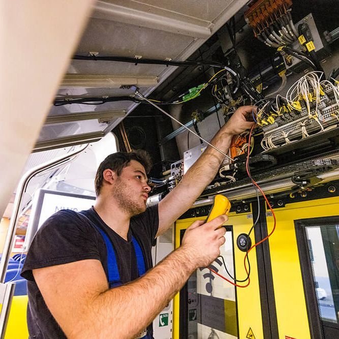 Junger Mann in Handwerker-Outfit arbeitet an der Türelektronik in einer Bahn.