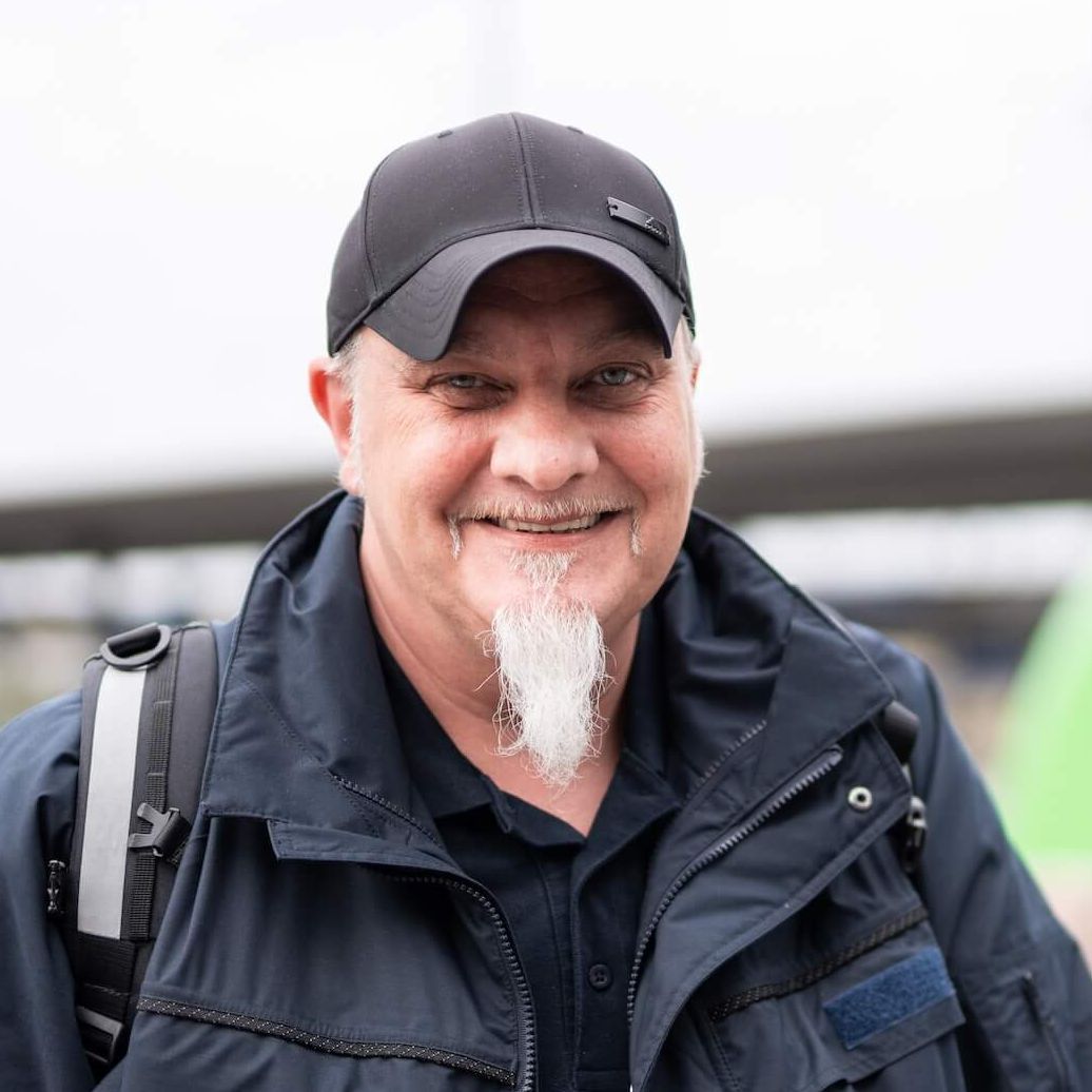 Lokführer Christian steht an einem Bahnsteig des Dortmunder Hauptbahnhofs. An einem Gleis im Hintergrund steht ein grün-weißer Zug.