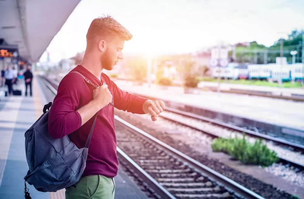 Mann steht an Bahnsteig und schaut auf die Uhr.