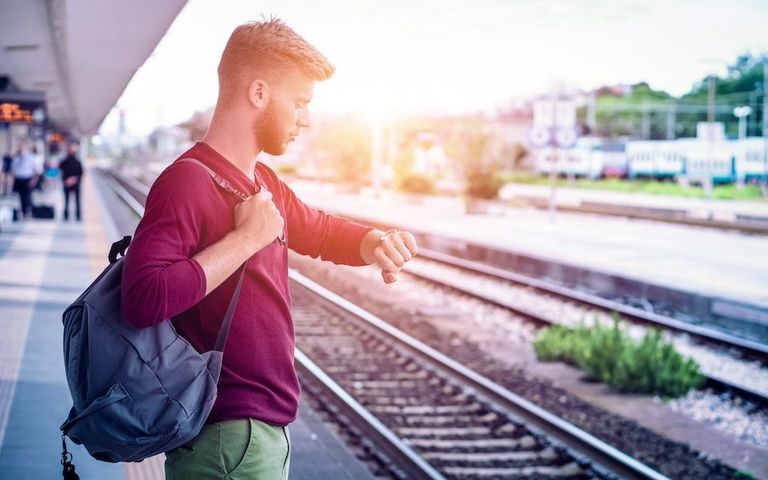 Mann steht an Bahnsteig und schaut auf die Uhr.