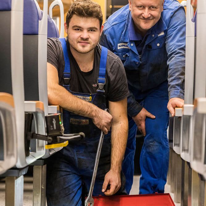 Zwei Mitarbeiter stehen vor einem geöffneten Boden eines Zugwaggons und reparieren etwas.