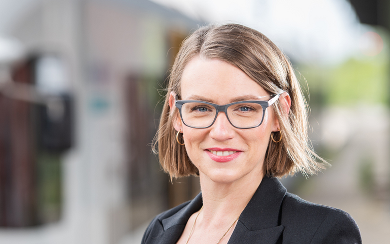 EIne Frau mit Brille und kurzen braunen Haaren steht vor einem Zug. 