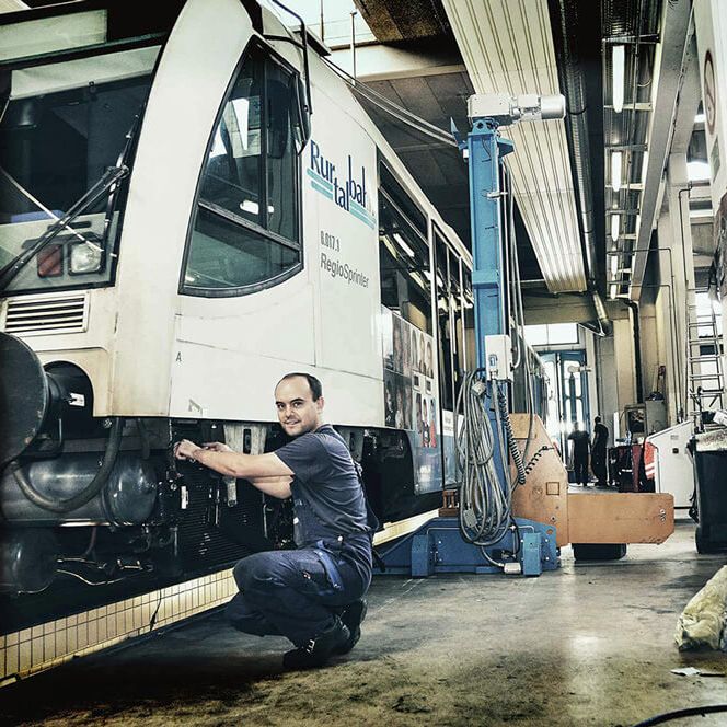 Ein Mann im Blaumann hockt in der Werkstatt neben einem Zug.