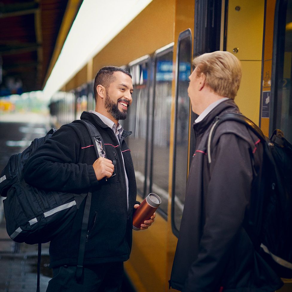 Zwei Lokführer stehen an einem Bahnsteig vor einem Zug und begrüßen sich mit einem Lächeln.