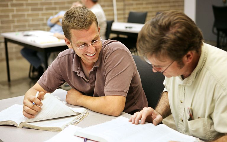 Erwachsene Schüler sitzen gemeinsam in einem Kurs und besprechen die vor ihnen liegenden Dokumente.