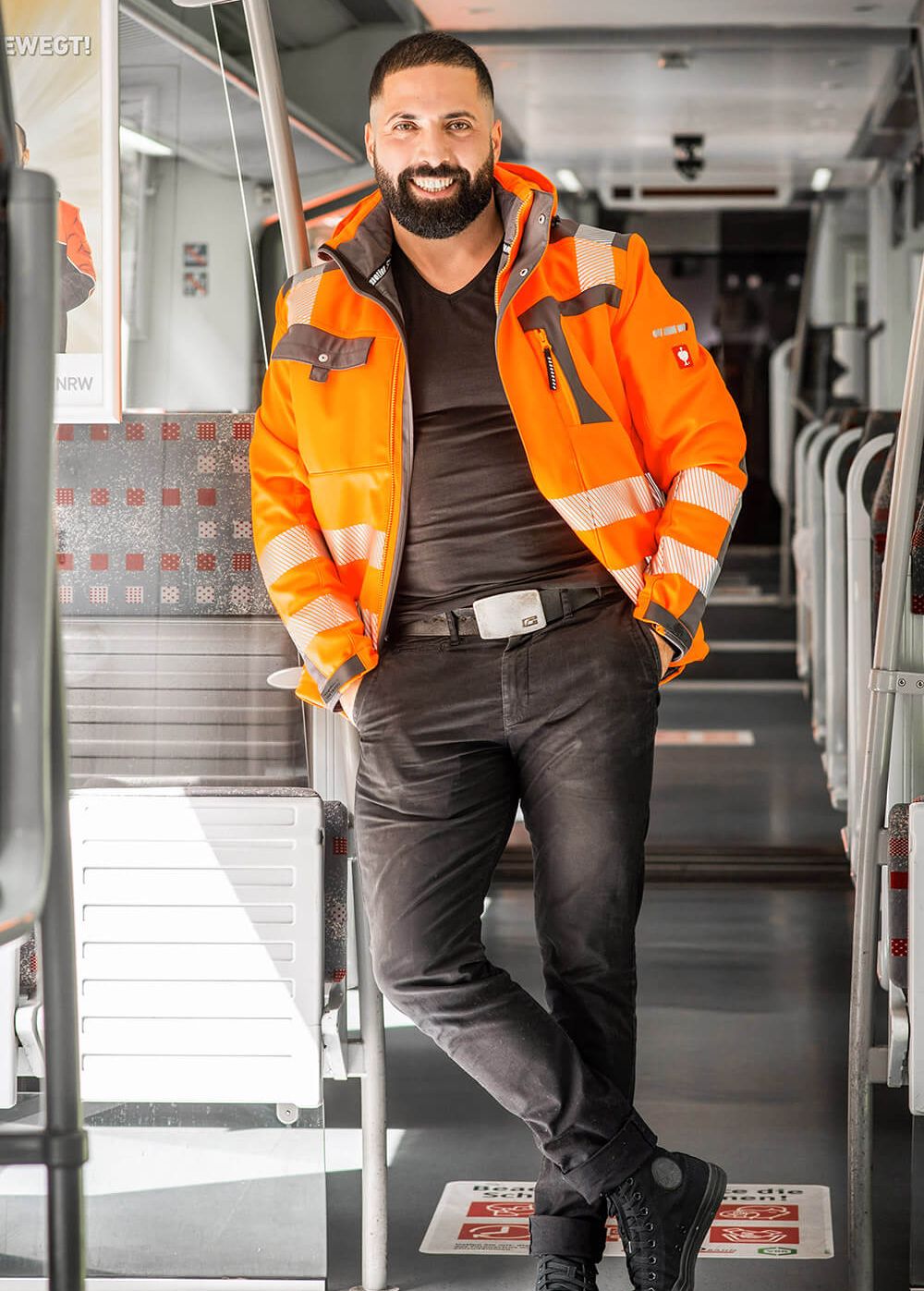 Zafer Kinik, Lokführer bei der Regiobahn, steht in einem Zug und lehnt sich lächelnd an eine Trennwand an.