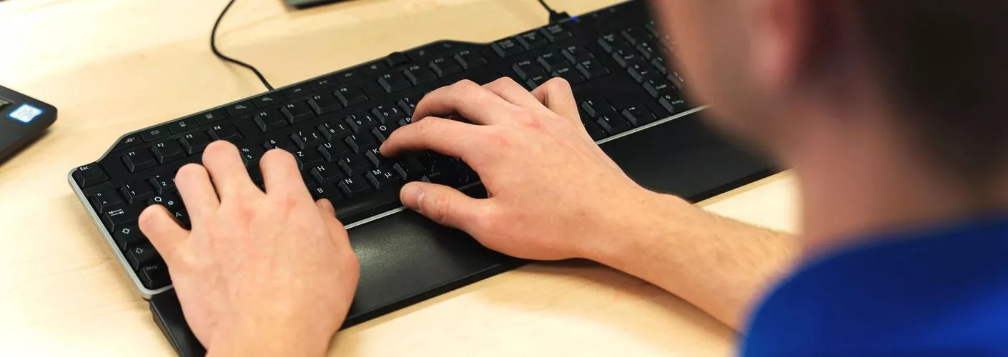 Marius tippt in seine Tastatur, der Kamerablick geht über seine linke Schulter, man sieht nur seine Hände und die Tastatur.