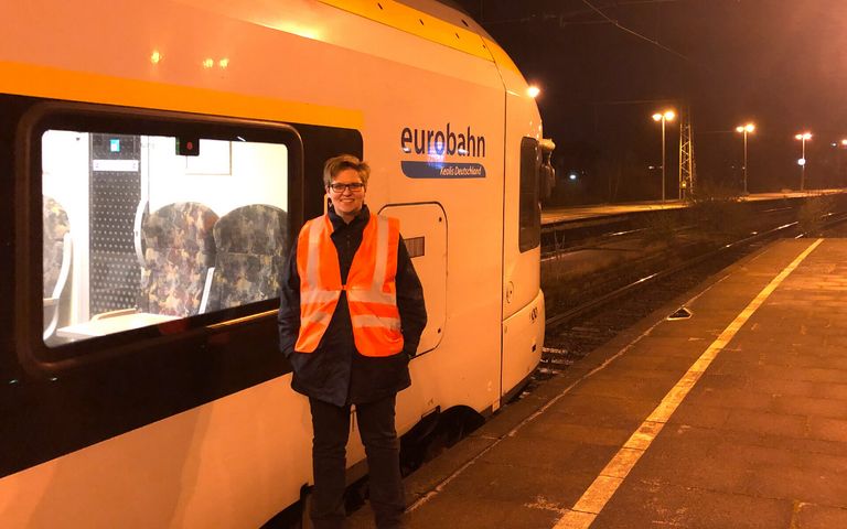 Lokführerin Corinna Dohmen steht bei Dunkelheit auf einem Bahnsteig, neben ihr steht ein Zug von eurobahn.