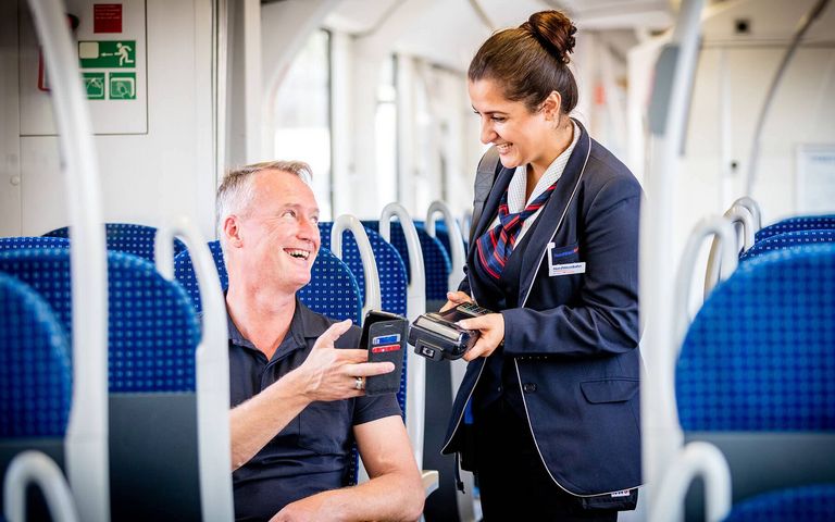 Eine Zugbegleiterin kontrolliert das Ticket eines Mannes, der in einem Zug sitzt.