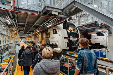 Mehrere Frauen gehen durch die Siemens-Werkhalle und passieren einen RRX, den die Frauen neugierig mustern.
