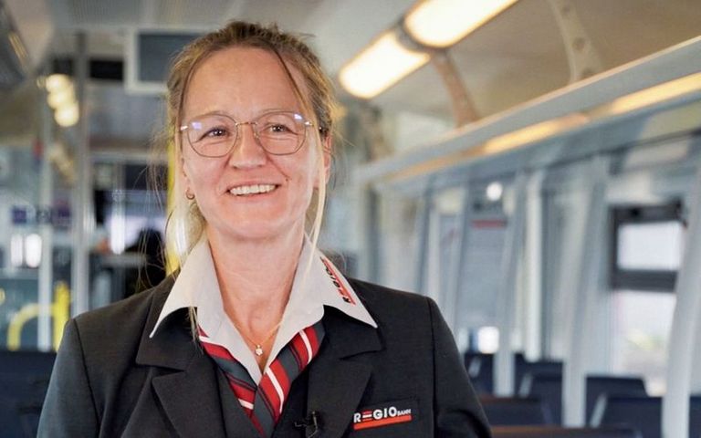 Eine Zugbegleiterin steht in einem Zugabteil und lächelt in die Kamera.