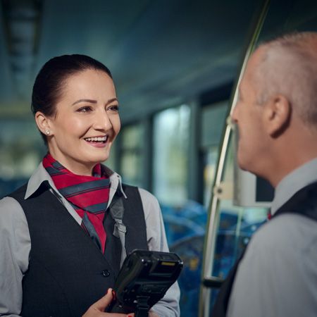 Eine Kundenbetreuerin spricht mit ihrem Kollegen. Beide befinden sich im Fahrgastraum eines Zuges und lächeln.