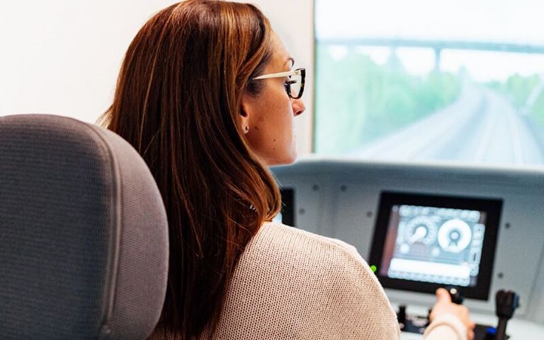 Eine Frau mittleren Alters mit Brille sitzt an einem Zugsimulator in einer Lokführer-Schule.