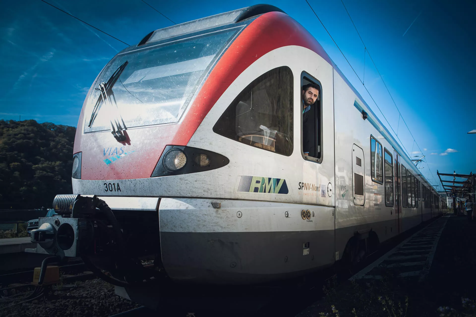 EIn Lokführer guckt aus dem Seiten-Cockpit-Fenster eines weißen Zuges, auf dem VIAS geschrieben steht.