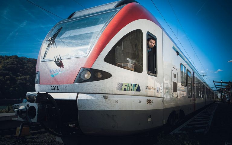 EIn Lokführer guckt aus dem Seiten-Cockpit-Fenster eines weißen Zuges, auf dem VIAS geschrieben steht.