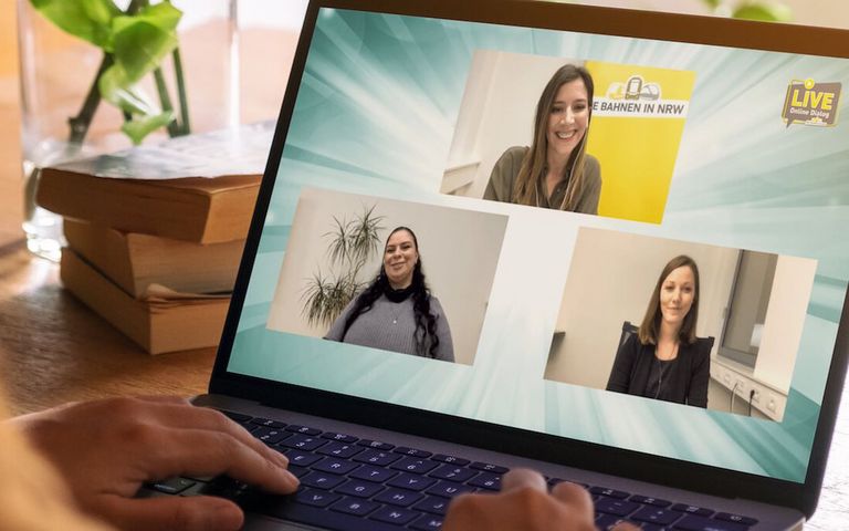 Eine Frau schaut auf ihren Laptop und sieht sich den Livestream an – drei junge Frauen sind auf dem Bildschirm zu sehen. 