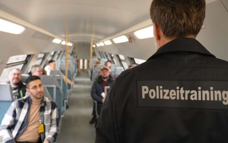 Ein Polizeibeamter steht mit Zuschauenden in einer Bahn.