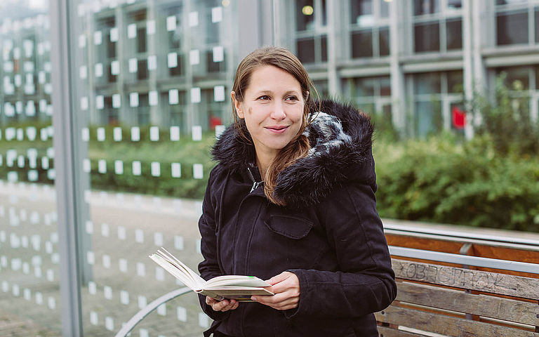 Sarah Meyer-Dietrich sitzt mit einem Buch in der Hand am Bahnsteig und schaut in die Ferne.