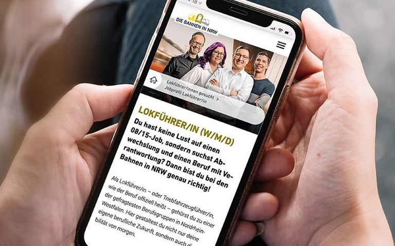 Ein Mann hält ein Handy in der Hand. Darauf betrachtet er das Lokführer*innen-Profil auf bahnen.nrw