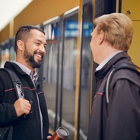 Zwei Lokführer unterhalten sich und stehen an einem Bahnsteig, an dem ein Zug hält. 