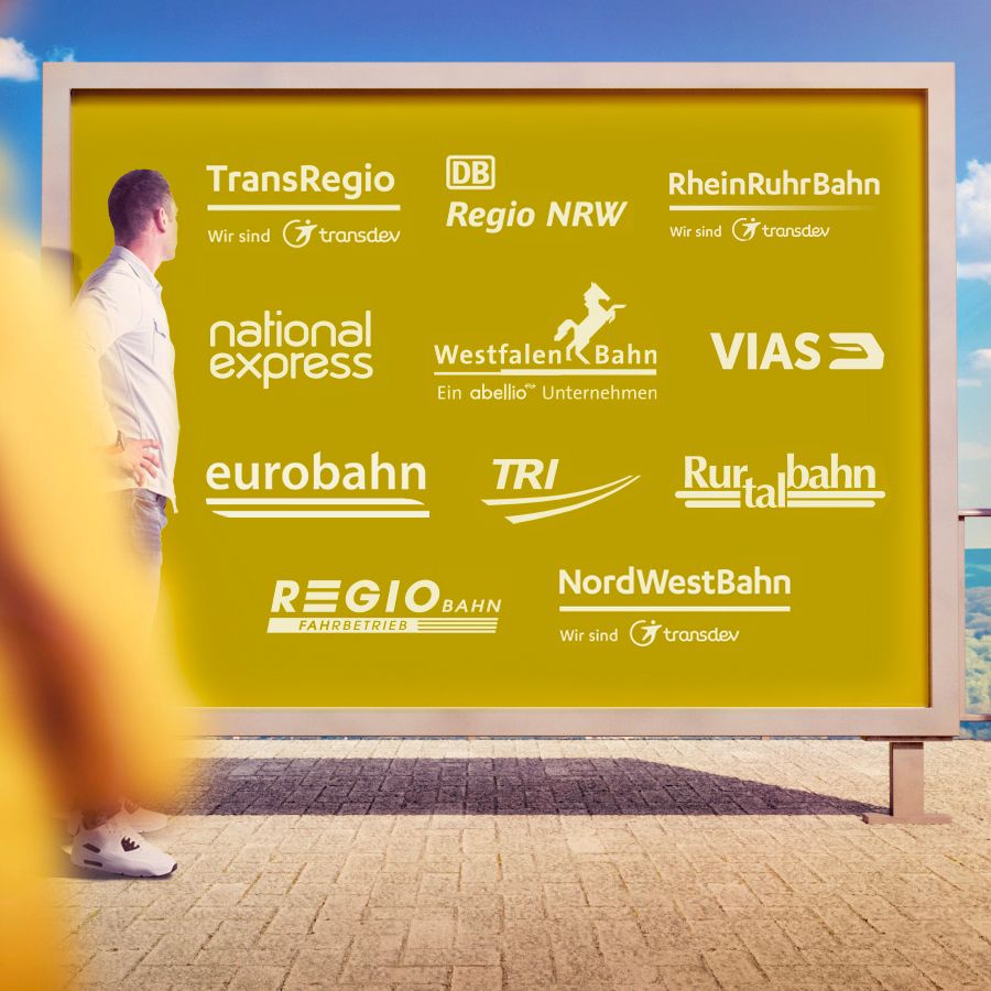 Frau im Vorder- und Mann im Hintergrund stehen vor einer goldfarbig unterlegten Tafel, auf der verschiedene Logos der Bahnunternehmen in NRW in weißer Farbe stehen.