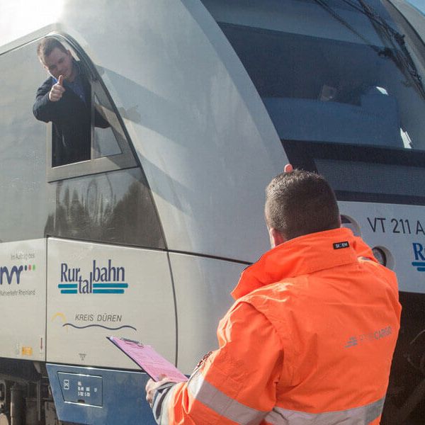 Triebfahrzeugführer in orangener Warnweste überprüft einen Zug und notiert sich Hinweise.