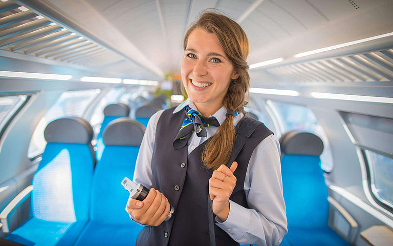 Eine junge Zugbegleiterin lächelt in die Kamera.