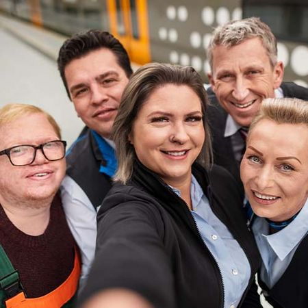 Eine Blonde Frau macht ein Selfie gemeinsam mit ihren Kolleg*innen – alle lächeln gemeinsam in die Kamera.