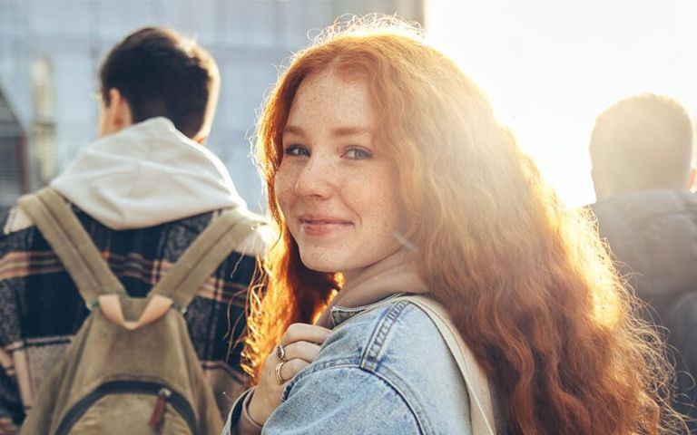 Eine junge Frau mit roten Haaren läuft hinter einer Gruppe von Jungs und schaut in die Kamera. 