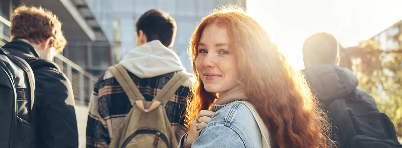Eine junge Frau mit roten Haaren läuft hinter einer Gruppe von Jungs und schaut in die Kamera. 