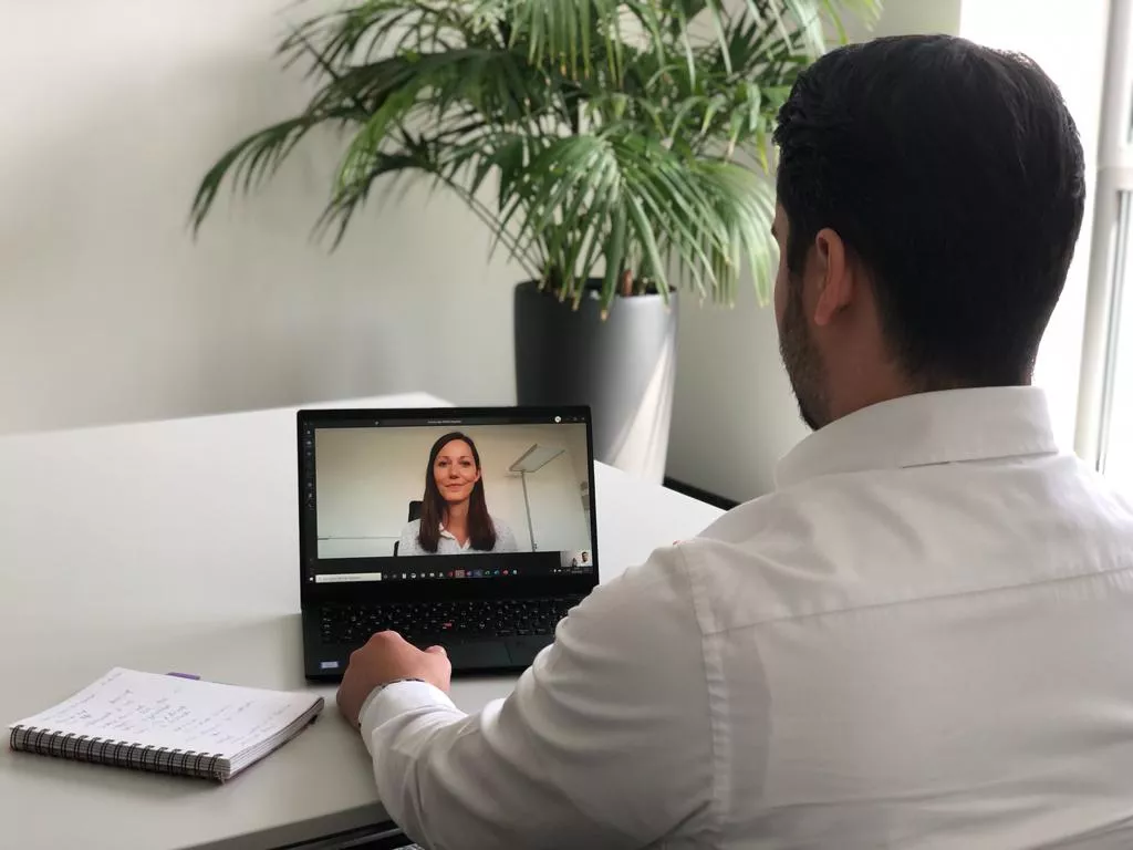 Ein Mann in einem Hemd führt ein Videointerview mit Sandra Grünefeldt.