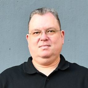 Triebfahrzeugführer Patrick posiert vor einer grauen Wand.