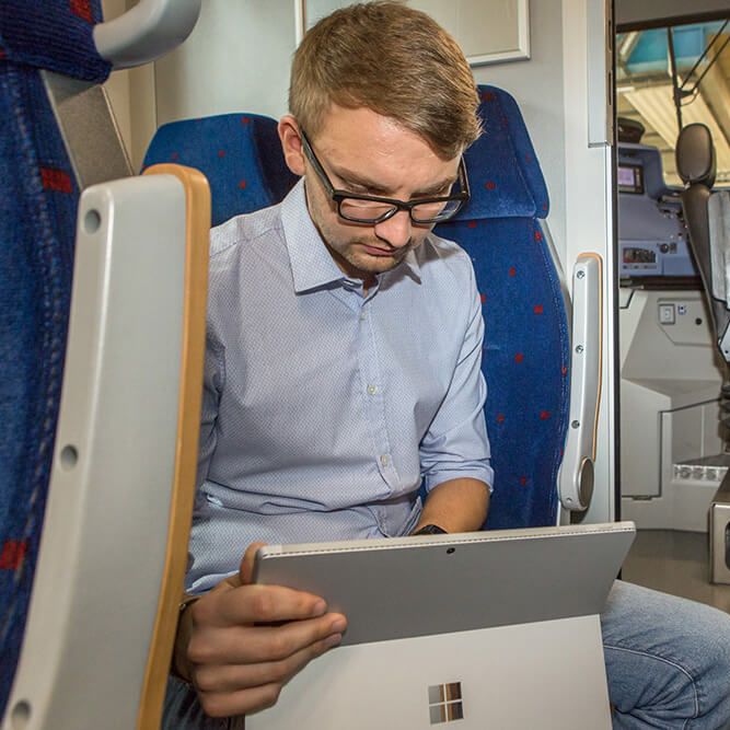 Ein Mitarbeiter schaut auf ein Tablet. Er sitzt in einem Zug und die Tür zum Führerstand steht offen.
