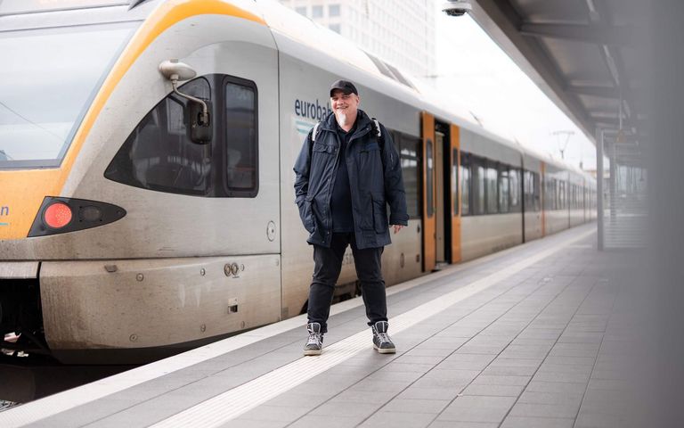 Lokführer Christian steht an einem Bahnsteig des Dortmunder Hauptbahnhofs. Hinter ihm am Gleis steht ein gelb-weißer Zug.